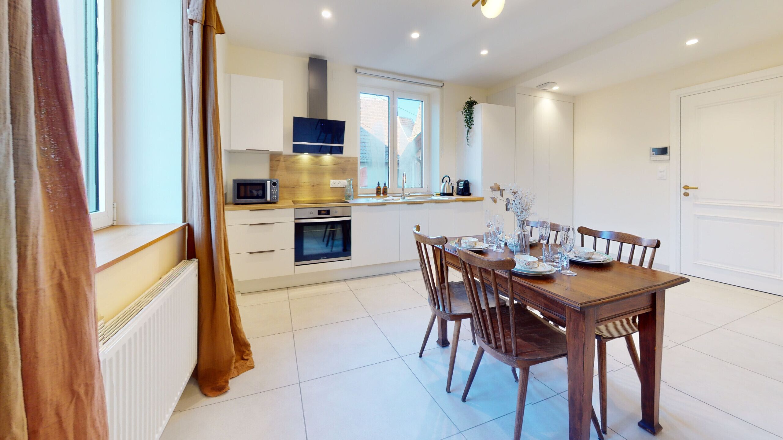 A modern kitchen with white cabinets, a microwave, and a dining area with a wooden table and chairs.