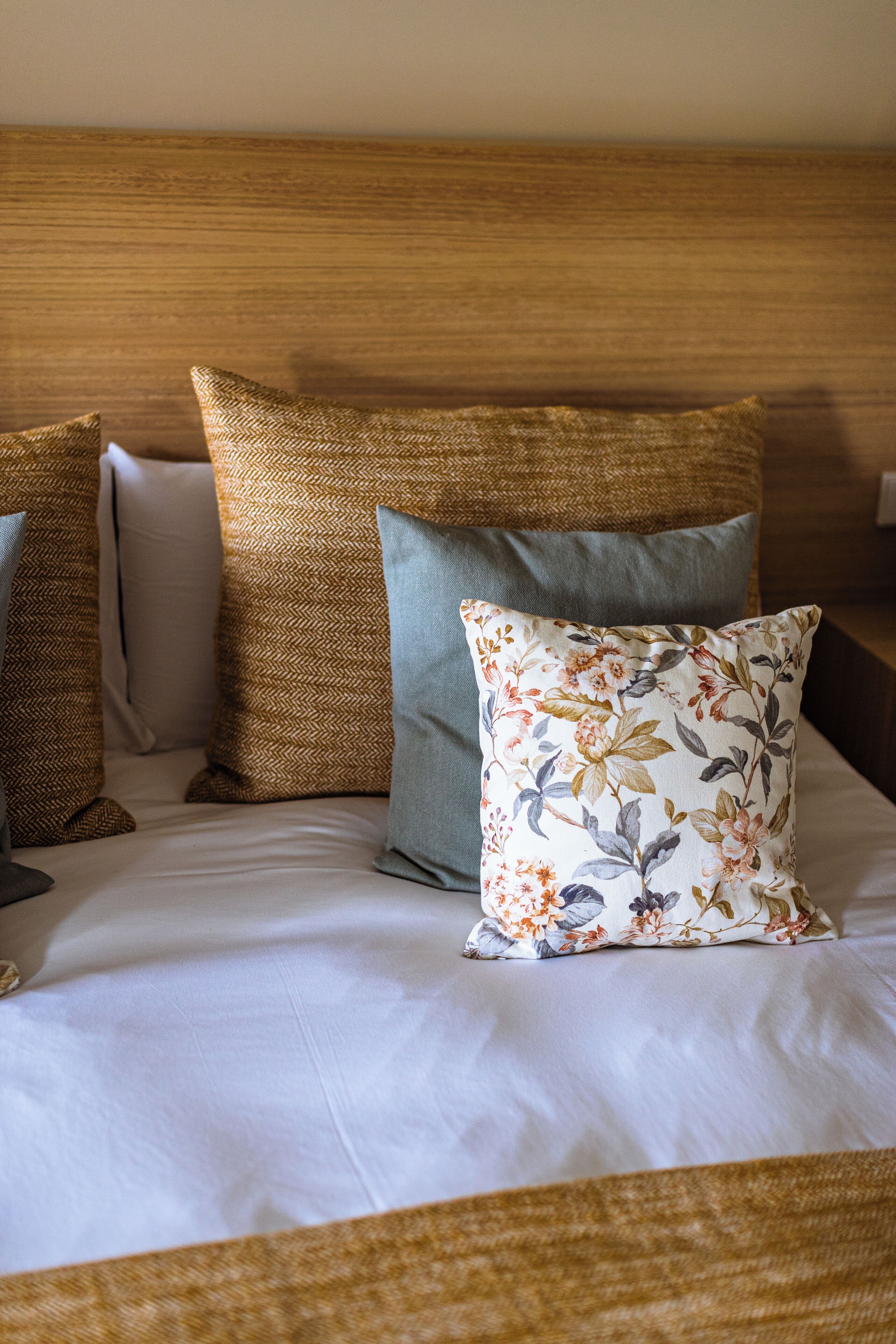 Una cama bien hecha con cuatro almohadas, un cabecero de madera y una colcha blanca.