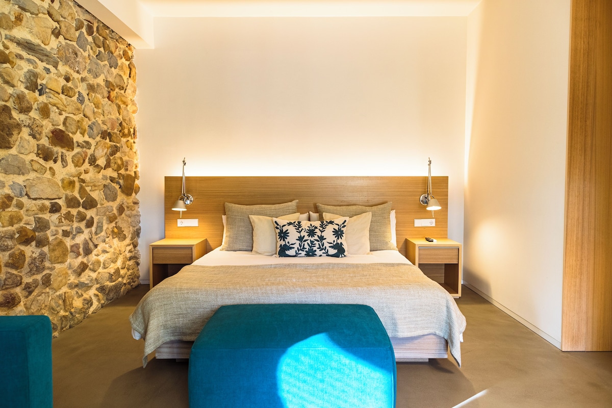 A bedroom with a stone wall, a wooden headboard, a bed with a floral pillow, and two bedside tables with lamps.