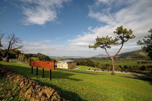 Un muro de piedra, un banco y un edificio con estacionamiento en un entorno rural.
