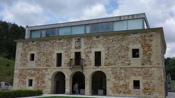 A stone building with a modern glass extension, featuring arched entrances and a balcony.