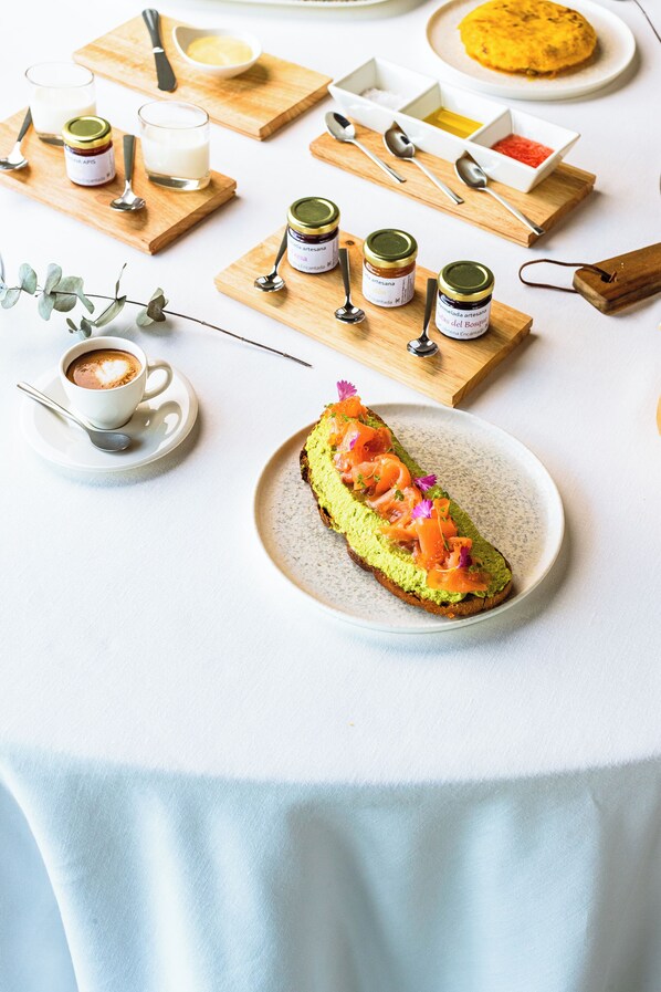 A table with a plate of avocado toast, a cup of coffee, and several condiments on wooden boards. - Hotel Pico Velasco (Voto)