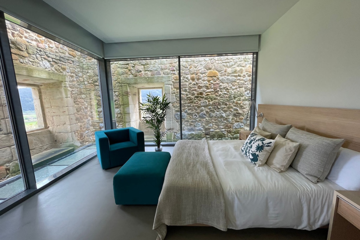 A bedroom with a large bed, a teal armchair, and a nightstand.