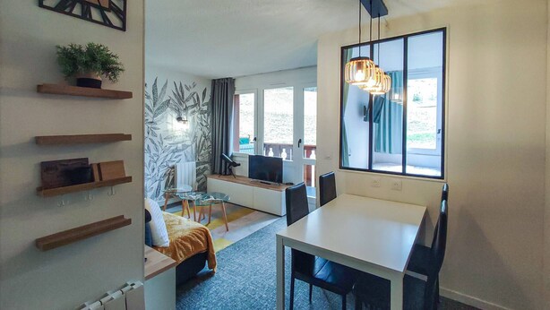 Een moderne woonkamer met een eethoek, een televisie en een groot raam.