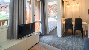 Een moderne hotelkamer met een groot flatscreen televisietoestel, een bed, een zithoek met tafel en stoelen, en uitzicht op een gebouw.