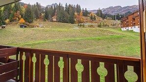 Een balkon met uitzicht op een grasveld, bomen met herfstkleuren en een berg op de achtergrond.