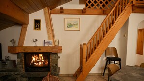 A cozy living room with a stone fireplace, wooden staircase, and a dining area.