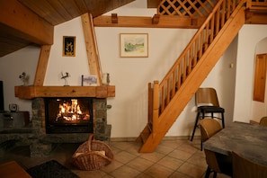 Un salon chaleureux avec une cheminée en pierre, un escalier en bois et un coin repas.