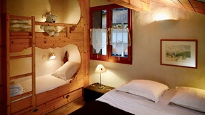 A wooden bunk bed room with a single bed, a nightstand with a lamp, and a window with curtains.