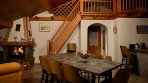 A cozy dining area with a stone fireplace, wooden staircase, and a dining table set for six.