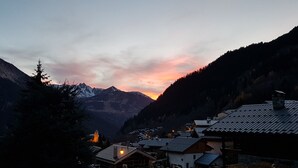 A mountain village at dusk with snow-capped peaks in the background and traditional houses with sloped roofs.