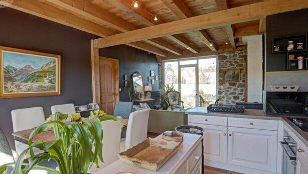 A rustic kitchen with white cabinets, a stone wall, and a dining area with a table and chairs. - Charming cottage near ski trails, 2 bedrooms (Saint-Régis-du-Coin)