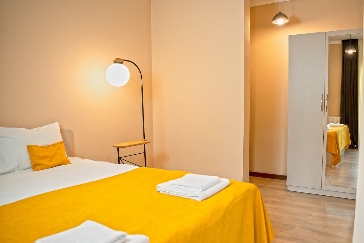 Quarto de hotel com cama, mesa de cabeceira, abajur e espelho.