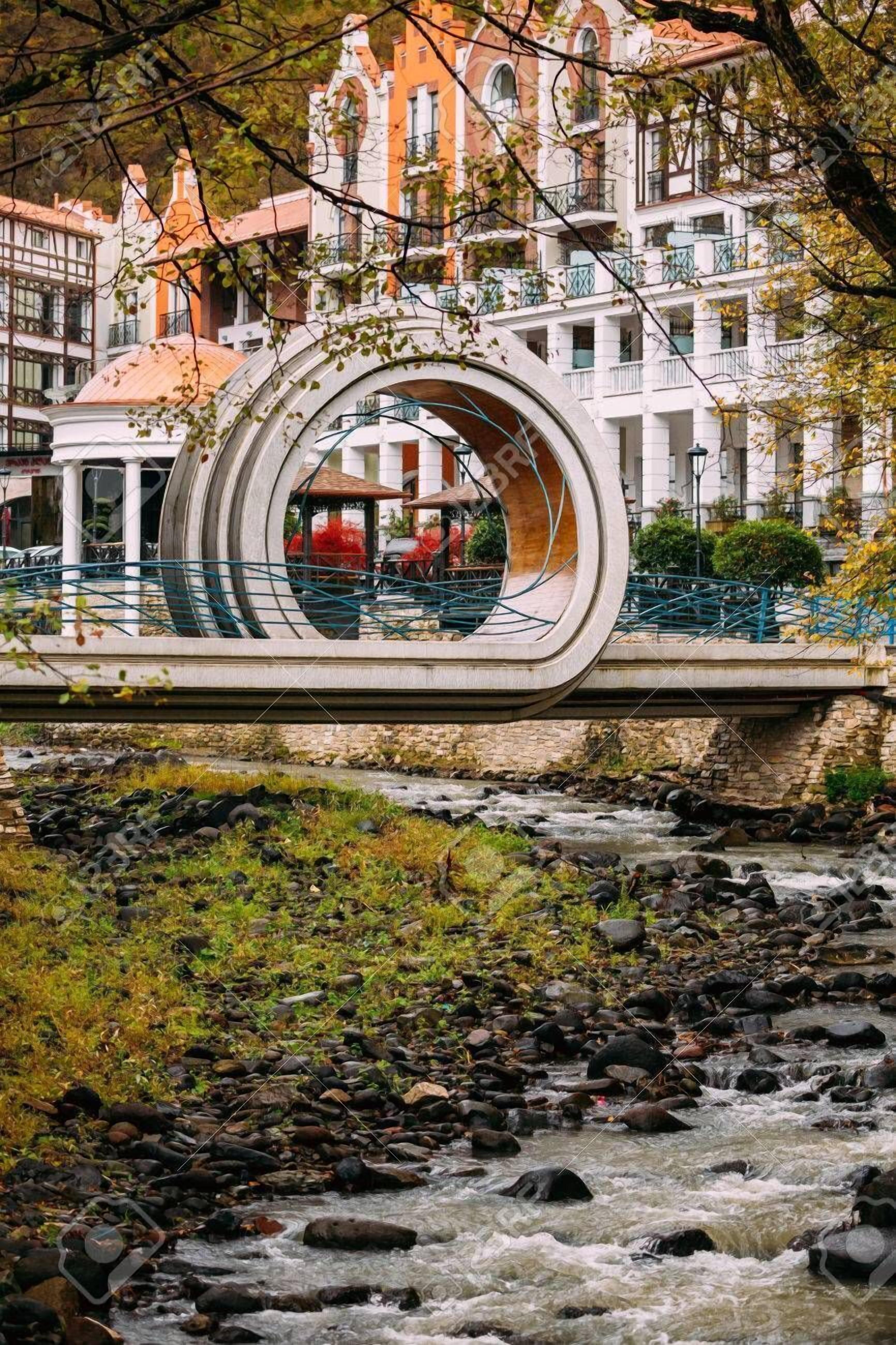 A modern bridge with a circular design over a flowing river, surrounded by historic buildings.