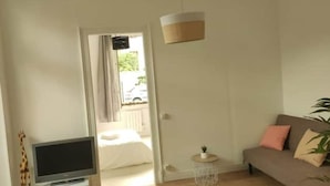 Un salon comprenant un canapé, un téléviseur, une petite table avec une plante et une porte-fenêtre donnant sur un balcon.