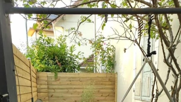 Un espace patio aménagé avec un hamac, des meubles en rotin noir et une clôture en bois.