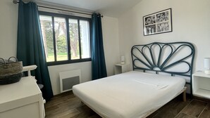 A bedroom with a bed, a dresser, a window with curtains, a bedside lamp, and a wall-mounted picture. - House in a very quiet area (Saint-Georges-d'Oléron)