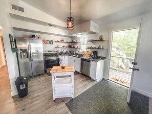 A compact kitchen with white cabinets, a stainless steel refrigerator, a wooden table, and a hanging light fixture. - 2nd floor, 2 bedroom, 2 bathroom unit near Boat Ramp 2 in Canyon Lake! (Canyon Lake)