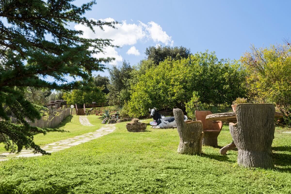 Un jardín con una vaca, un banco de piedra y un tocón de árbol.