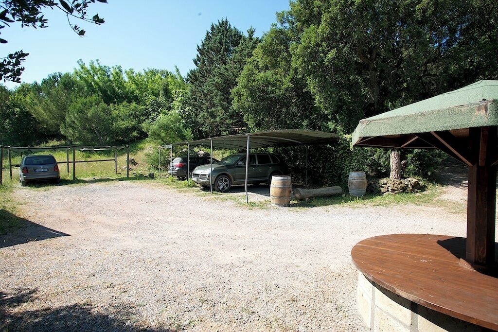 A gravel parking area with a covered carport and a wooden bench.