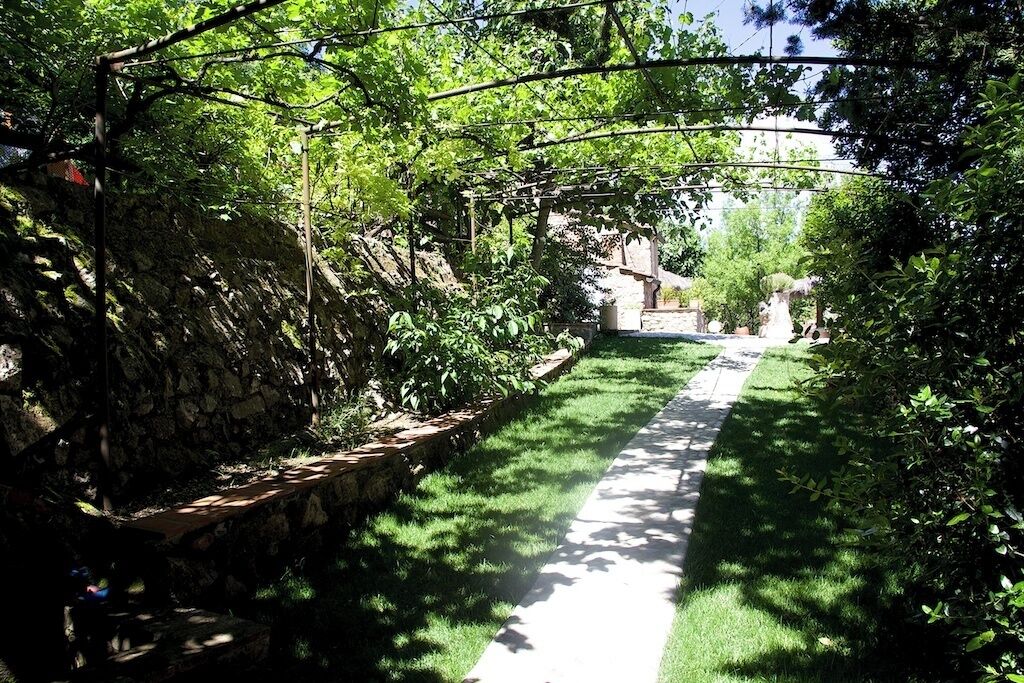 A pathway flanked by lush greenery and stone walls, leading to a building with a statue.
