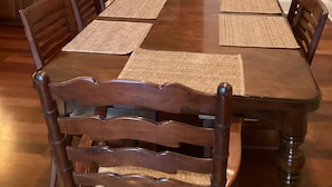A dining area with a long wooden table and matching chairs, a kitchen with wooden cabinets and stainless steel appliances, and a tiled backsplash.