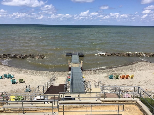 Ein Strand mit einer Pier, die ins Wasser führt, umgeben von Stühlen und einer felsigen Küste.