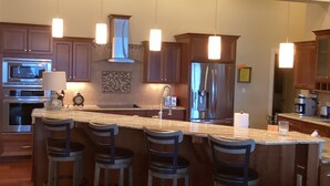 A modern kitchen with a central island, bar stools, stainless steel appliances, and pendant lighting.