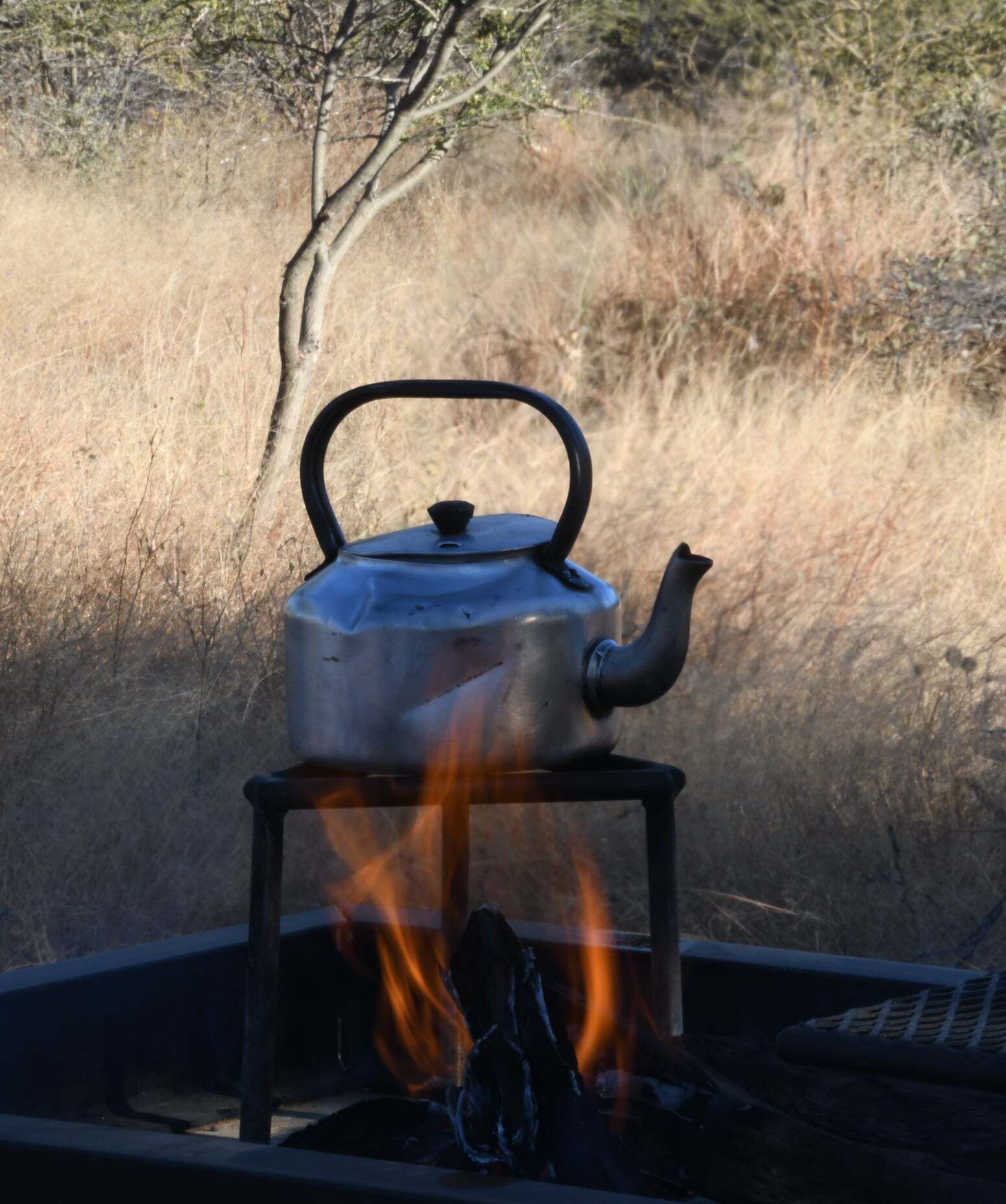 A kettle on a portable stove with flames.