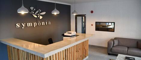Zona de recepción con un mostrador de madera, dos lámparas colgantes, un sofá y una mesa de centro.