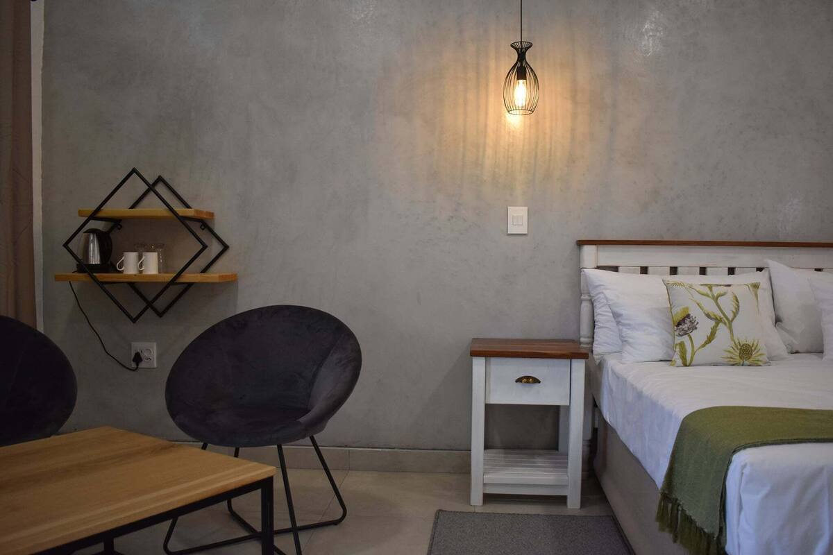 A bedroom with a bed, bedside table, chair, and a wall-mounted shelf.