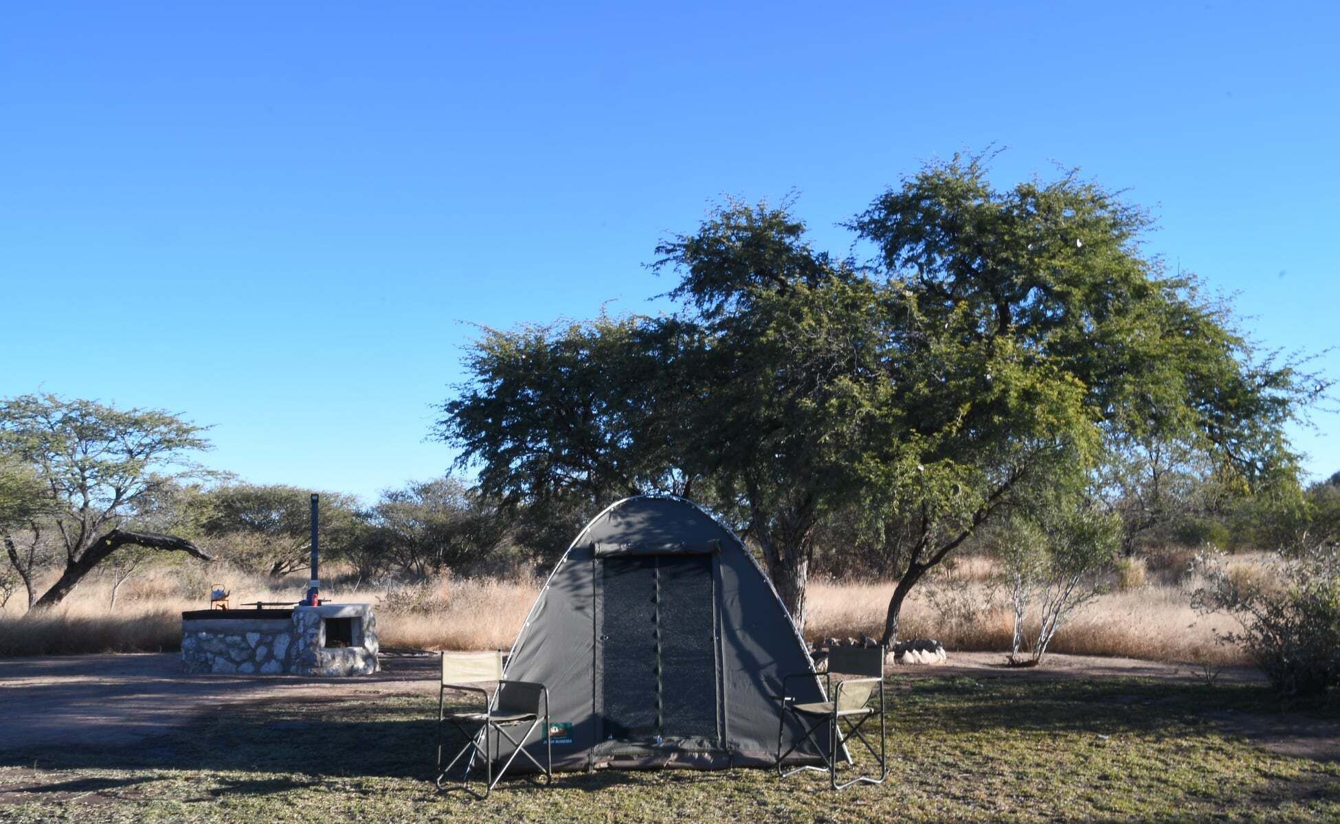 A camping site with a tent, two chairs, and a stone structure.