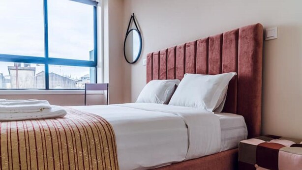 Hotellihuone, jossa on sänky, ikkuna ja näkymä kaupunkiin.