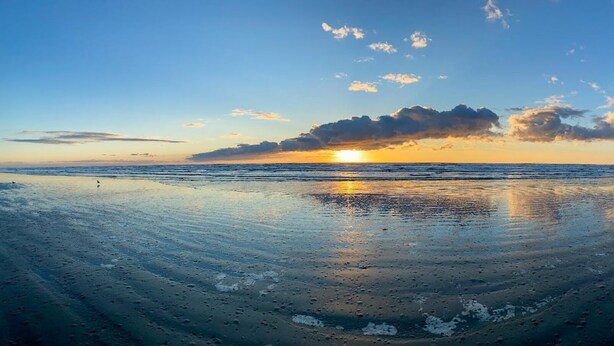 A beach at sunset with calm waves and a clear sky.
