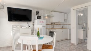 Una cocina moderna con armarios blancos, una mesa de comedor con sillas, un televisor montado en la pared y un microondas en la encimera.
