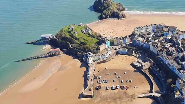 An aerial view of a coastal town with a beach, a fortified structure, and a pier.