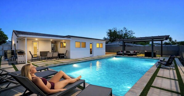 A poolside area with lounge chairs, a barbecue grill, and a covered patio. - Retreat Near MIA • Heated Pool_BBQ & Playground (Miami)