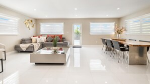 A spacious living room with a grey sofa, a coffee table, and a dining area with a wooden table and chairs. - Retreat Near MIA • Playground & Heated Pool, BBQ (Miami)