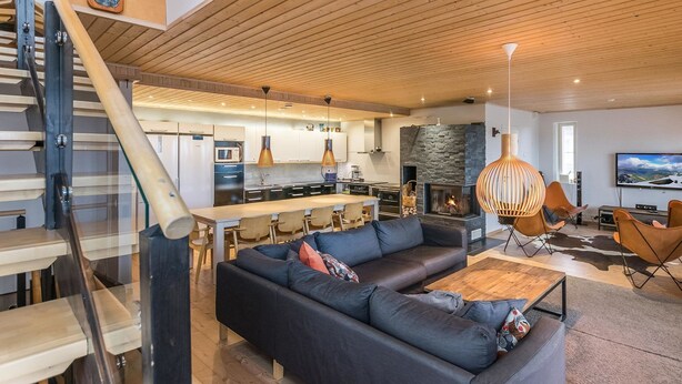 Een moderne woonkamer met een grote bank, een eethoek en een keuken op de achtergrond.
