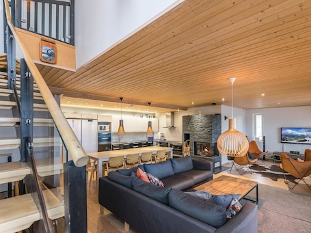 A modern living room with a large sofa, a dining area, and a kitchen in the background.