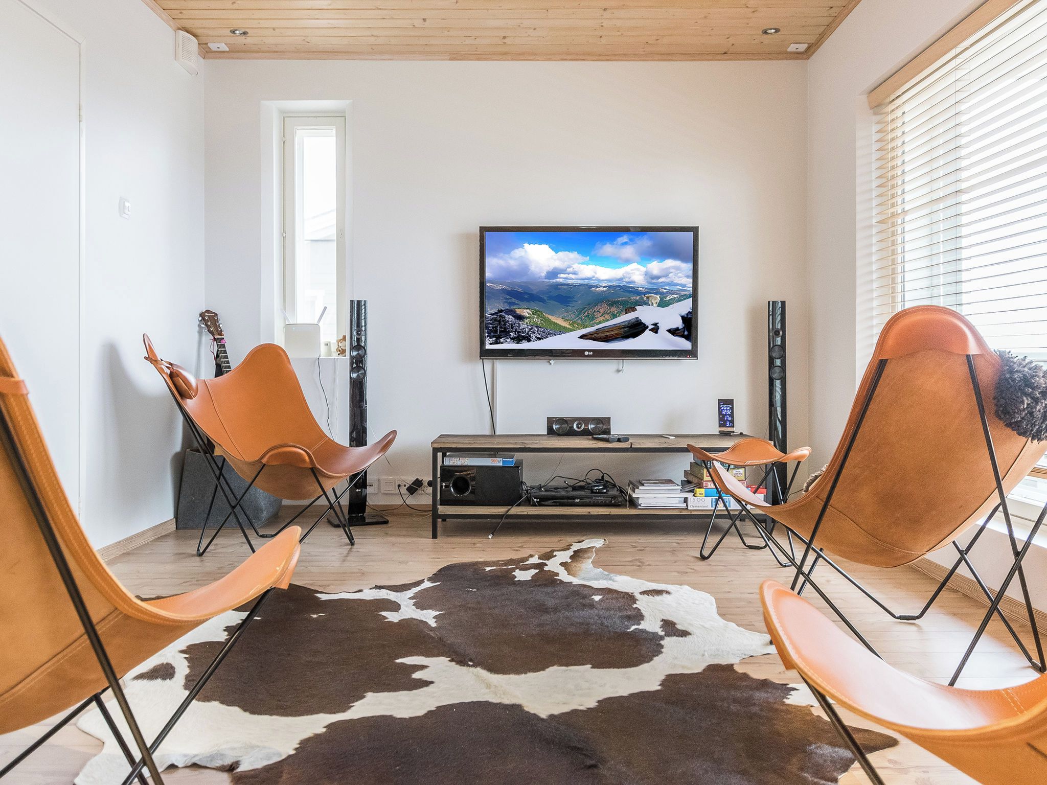 Uma sala de estar moderna com uma TV de tela plana na parede, um móvel para home theater em madeira e duas poltronas de couro.
