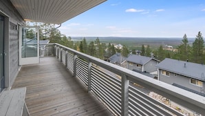 Een houten terras met een glazen deur die leidt naar een balkon met uitzicht op een woongebied met huizen en bomen.