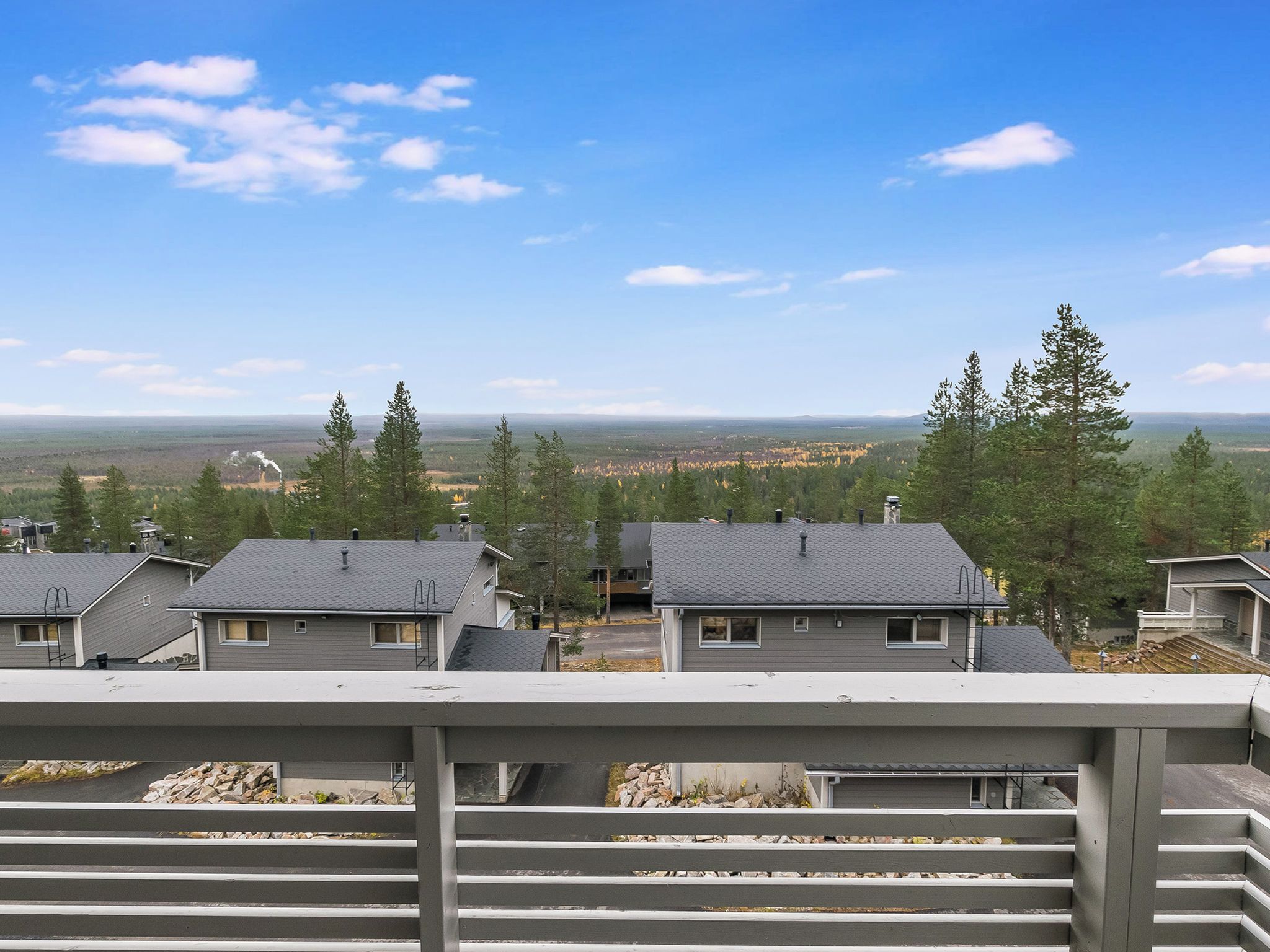 Área residencial com várias casas, céu claro e uma vista distante de uma paisagem arborizada.