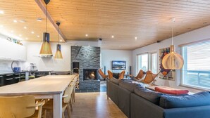 Een moderne woonkamer met een open haard, houten plafond en een eetgedeelte met een lange tafel en stoelen.