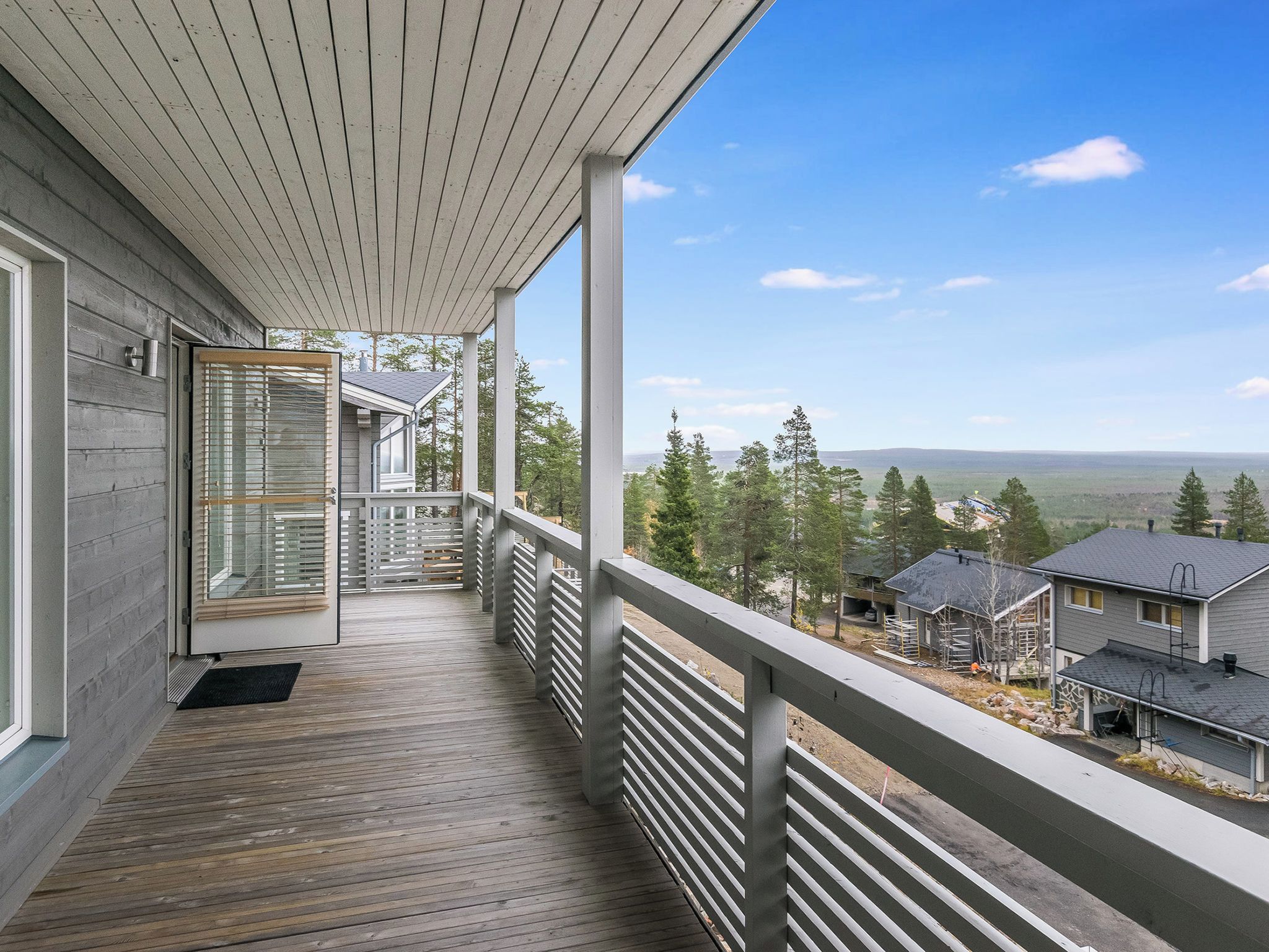 A wooden deck with a railing, a door with glass panels, and a view of houses and trees.