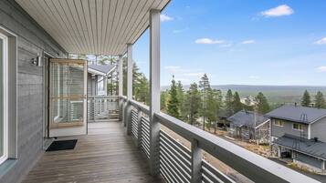A wooden deck with a railing, a door with glass panels, and a view of houses and trees.
