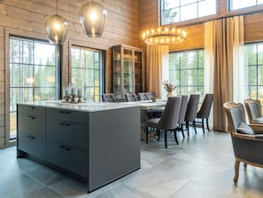 Een ruime keuken met een groot eiland, moderne apparatuur en grote ramen met uitzicht op het omliggende bos.