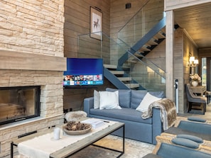 Een moderne woonkamer met een stenen muur, een open haard, een blauwe bank en een trap.