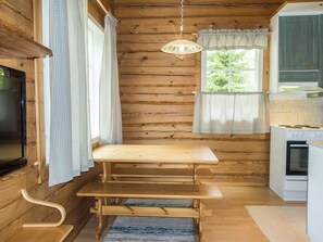 A wooden cabin interior with a wooden table and bench, a television, a window with curtains, and a kitchen area with a stove. - Kranni 2 by Interhome (Pudasjärvi)