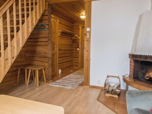Interior de una cabaña de madera con escalera, chimenea y una pequeña mesa.